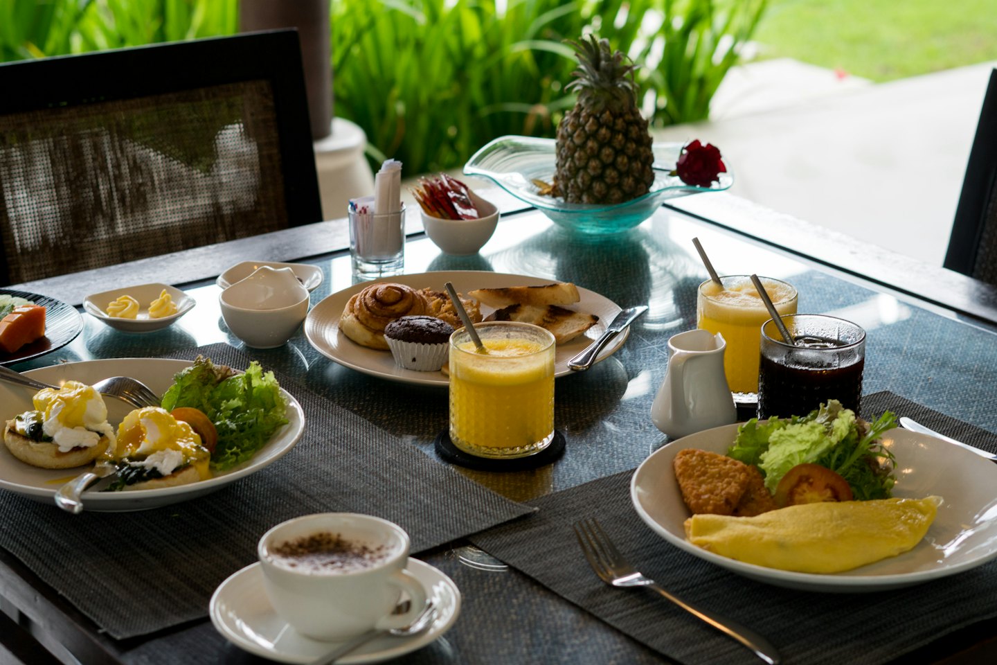 Colazione per due con uova, pasticcini, frutta e caffè su un tavolo da esterno.